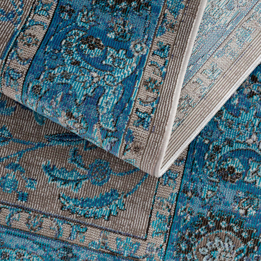 Close-up of the Mardina Turquoise Area Rug showing its beige and turquoise traditional vintage pattern and machine woven texture. Fold