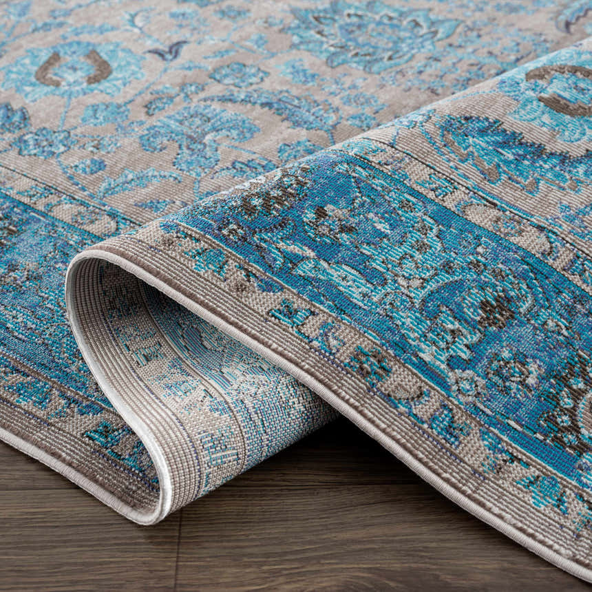 Close-up of the Mardina Turquoise Area Rug showing its vintage floral pattern and texture in beige and turquoise. Fold