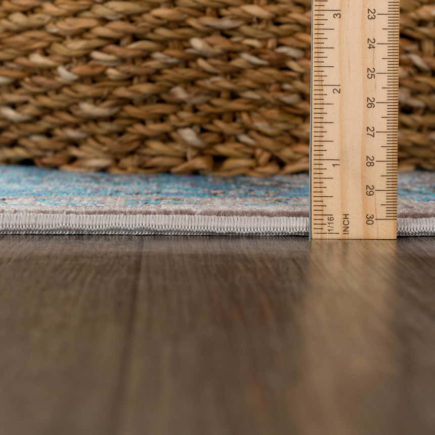 Close-up of the Mardina Turquoise Area Rug showing the rug's pile height with a ruler and a woven basket in the background. Pile