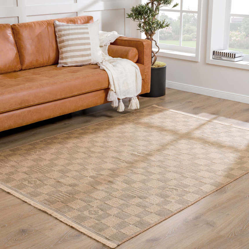 Living room scene with a beige Nairi Checkered Washable Jute Rug, brown leather sofa, and natural light from a window. Roomscene-Rectangle