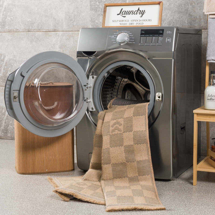 Laundry room scene with a beige and black Nairi Checkered Washable Jute Rug partially inside the washing machine. Washing-Machine