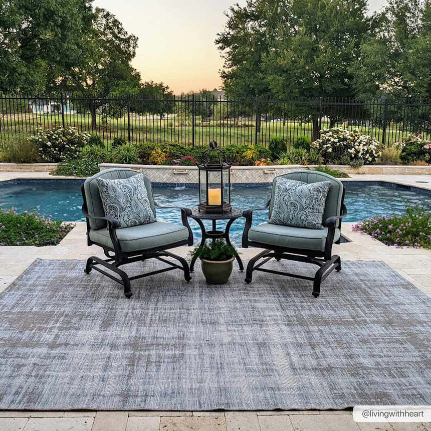Outdoor patio scene with Manzanita Area Rug in blue and cream, two chairs, side table, and pool in the background. Roomscene-Rectangle