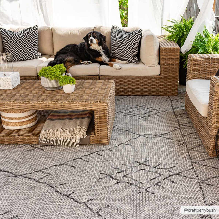Outdoor patio scene with wicker furniture and a gray Marwood Nordic Performance Rug with a geometric pattern. A dog relaxes on the sofa. Roomscene-Rectangle