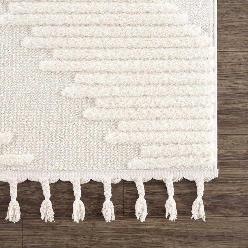 Close-up of the Palimbang Cream 3D Rug. Features a geometric pattern, plush texture, and braided tassels on a wood floor. Swatch