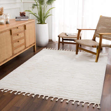 Living room scene with a cream Kulu Textured Area Rug with Tassels, wooden furniture, and a tall potted plant. Roomscene-Rectangle