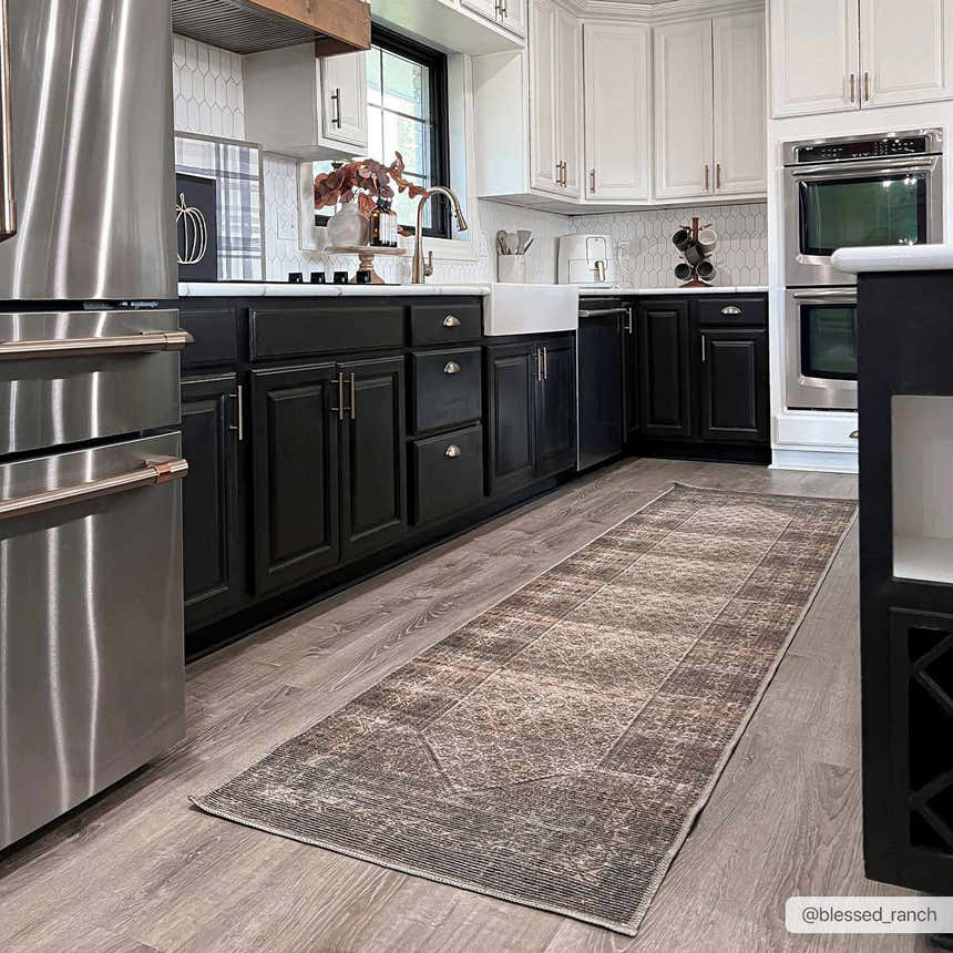 Farmhouse kitchen with a Tan Ormstown Distressed Washable Area Rug runner on wood floors. Black and white cabinets. Roomscene-Runner