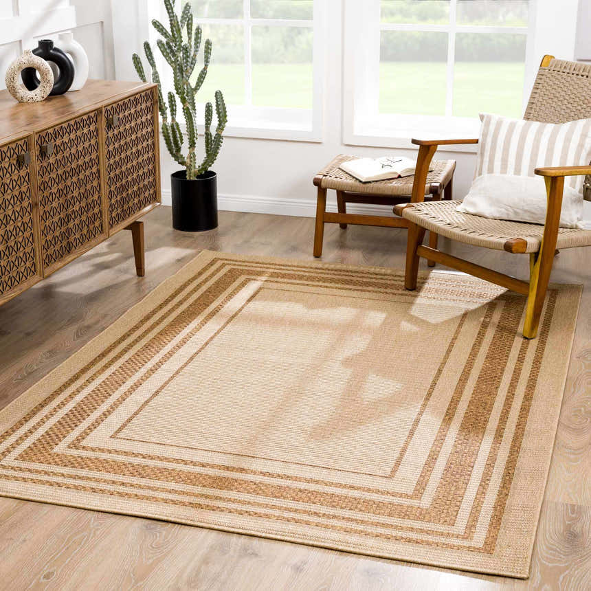 Living room scene with a camel Isoko Bordered Faux Jute Rug, wooden furniture, and a cactus near a bright window. Roomscene-Rectangle