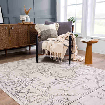 Cozy living room scene with a Divya Cream & Charcoal Area Rug, gray chair, wood cabinet, and natural light. Southwestern style. Roomscene-Rectangle