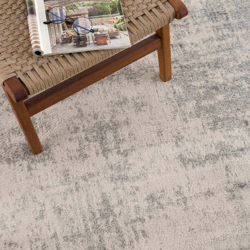 Close-up of the Kalanganan Abstract Gray Rug showing its texture and pattern next to a wooden chair with a magazine. Styleshot