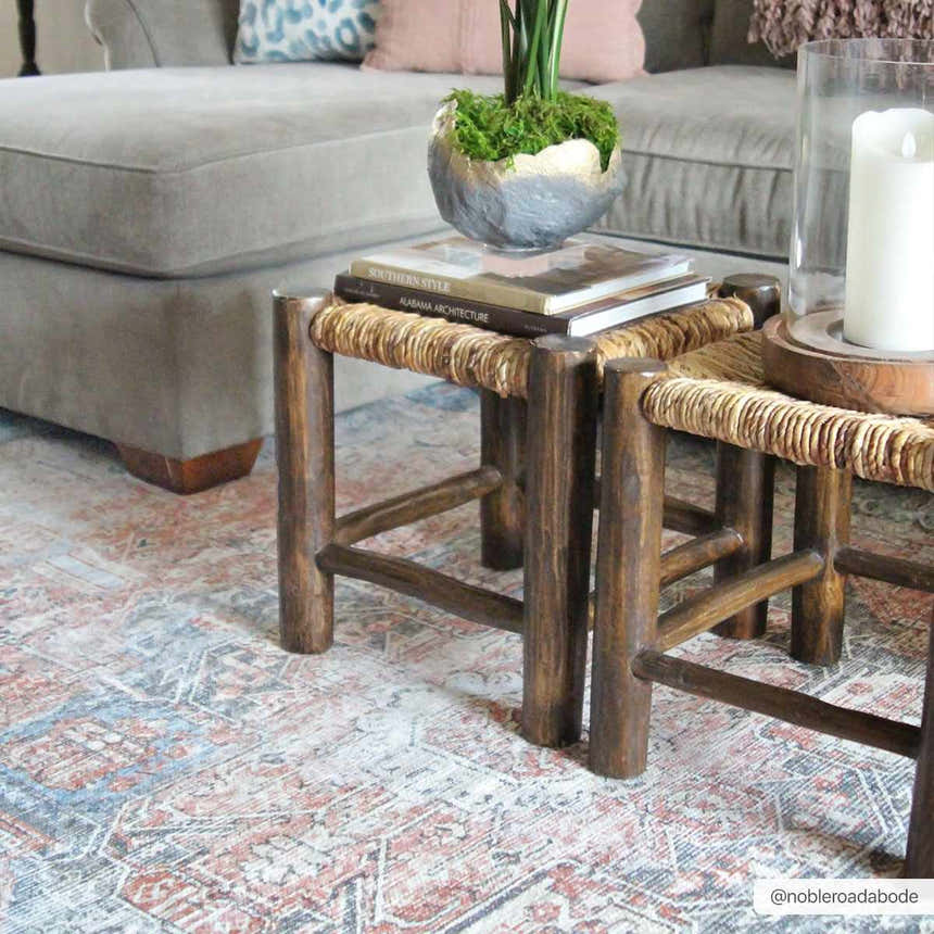 Living room scene with a Rosman Distressed Washable Area Rug in beige, blue, and brick red under rustic wood stools. Roomscene-Rectangle