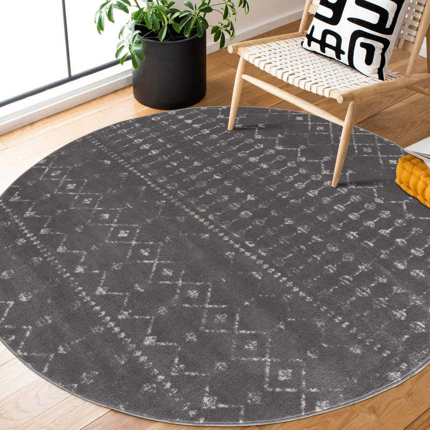 Round Tigrican Charcoal 2329 area rug in a modern living room with a chair, plant, and wood floors. Roomscene-Round