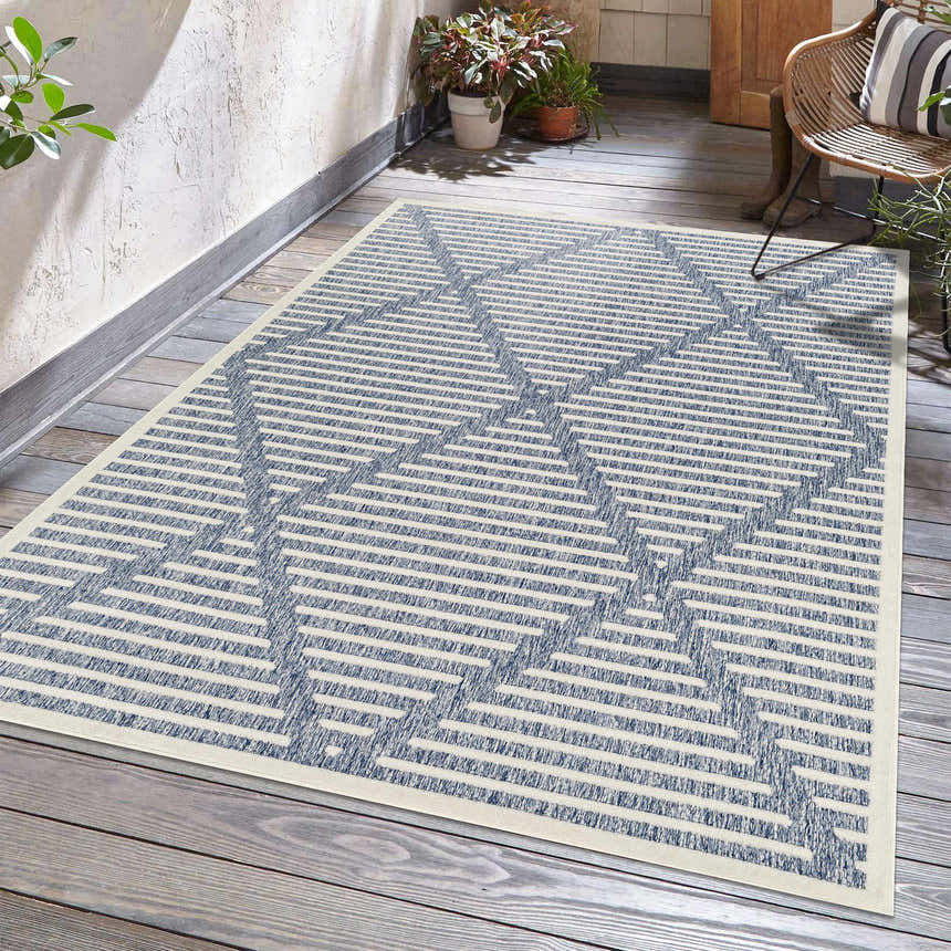 Outdoor patio scene with Anah Blue rug, wood floors, rattan chair, and plants. Roomscene-Rectangle