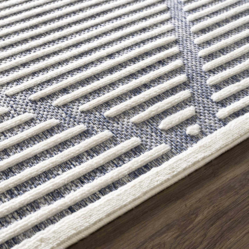 Close up of the Anah Blue Outdoor Rug showing the textured white stripes and blue woven background. Styleshot