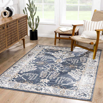 Living room scene with a denim blue Scalby Area Rug, wood cabinet, and woven chairs near a bright window. Roomscene-Rectangle