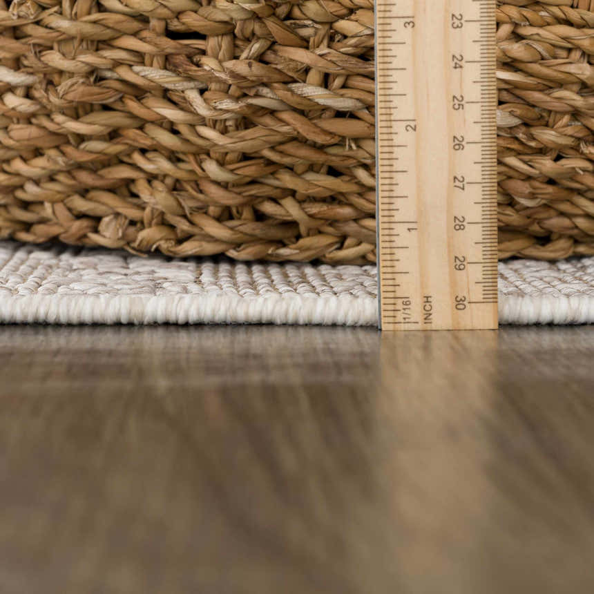 Close-up of Baqer Bone & Tan Textured Performance Rug showing pile height and texture next to a woven basket. Pile