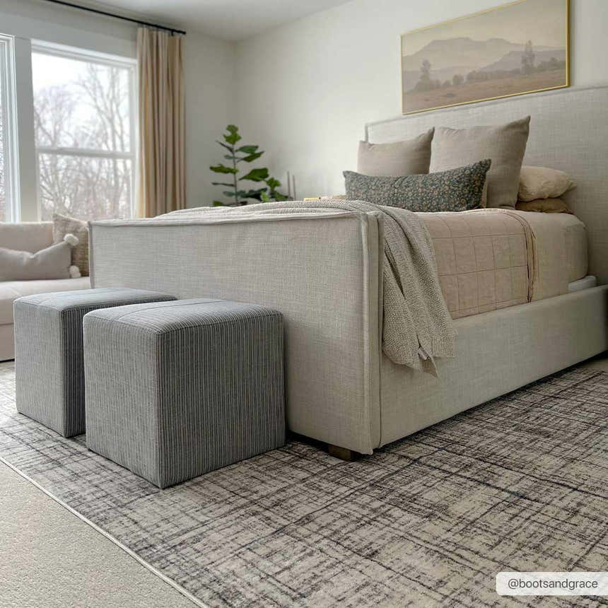 Bedroom scene with a Taysan Area Rug in dark gray, purple, and taupe, complementing the neutral tones of the furniture. Roomscene-Rectangle