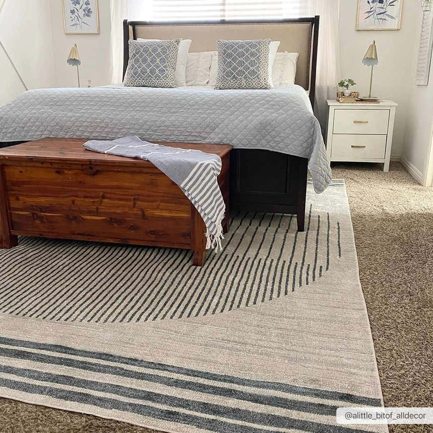 Bedroom scene with a Thad Medium Gray Washable Area Rug, wood chest, gray bedding, and white nightstand. Modern, cozy style. Roomscene-Rectangle