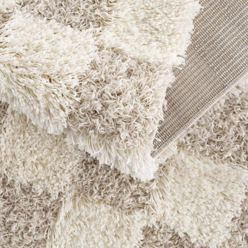 Close-up of the Atira Light Brown Checkered Area Rug showing its cream and light brown shag texture and woven backing. Fold