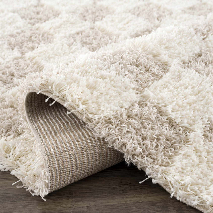 Close-up of the shag Atira Light Brown Checkered Area Rug, showing cream and light beige geometric pattern and soft texture. Fold