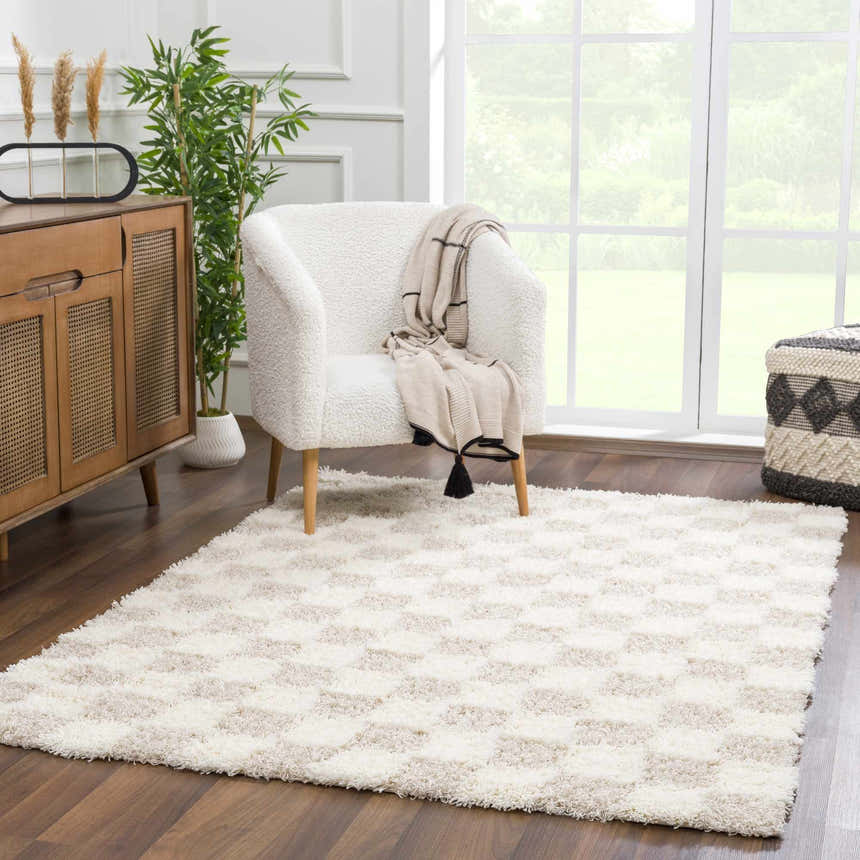 Living room scene with Atira Light Brown Checkered Area Rug, white chair, wood cabinet, and large window. Neutral tones. Roomscene-Rectangle