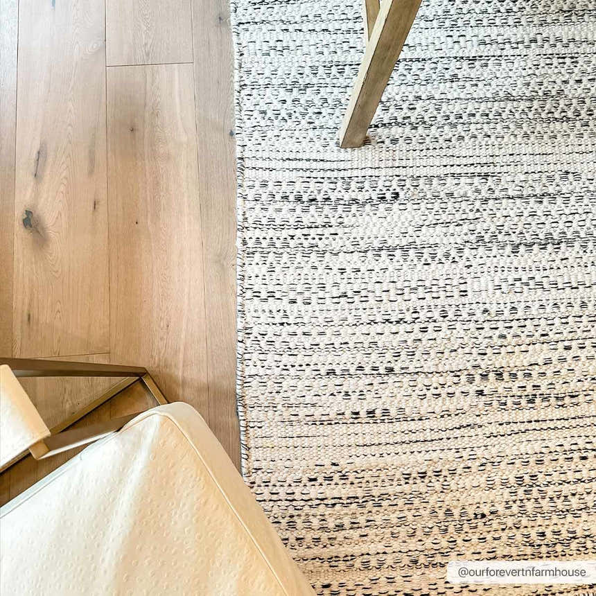 Close-up of the hand-woven Williford Wool Area Rug in cream and black, styled with a chair and table on hardwood floors. Styleshot