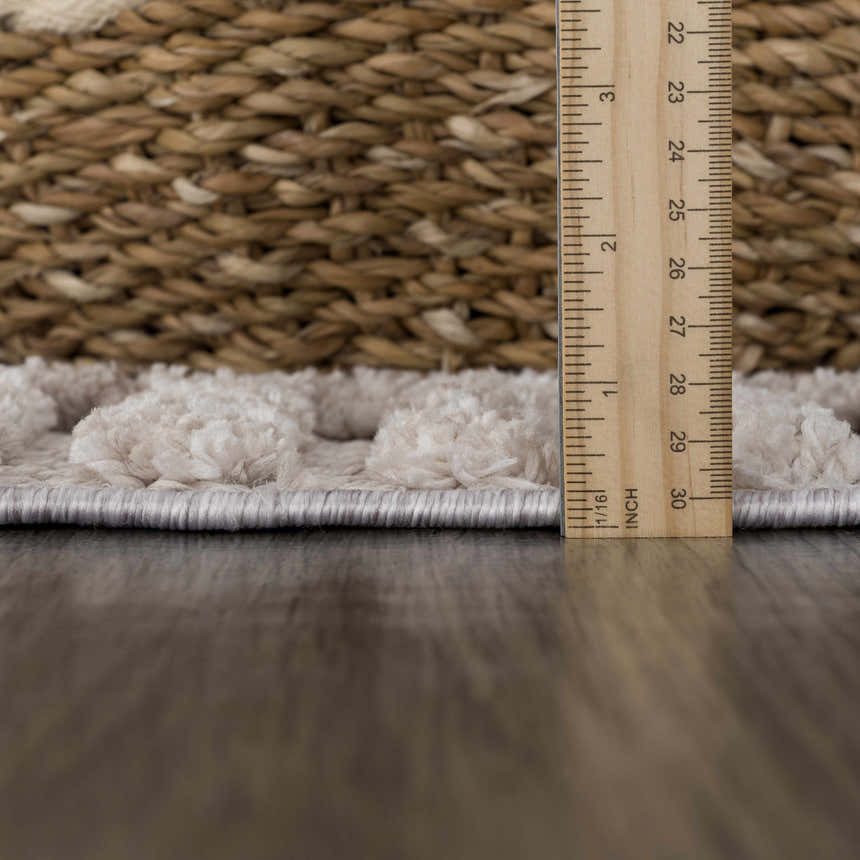 Close-up of the Amaga High-Low Rustic Rug showing its cream geometric design, texture, and pile height with a ruler. Pile