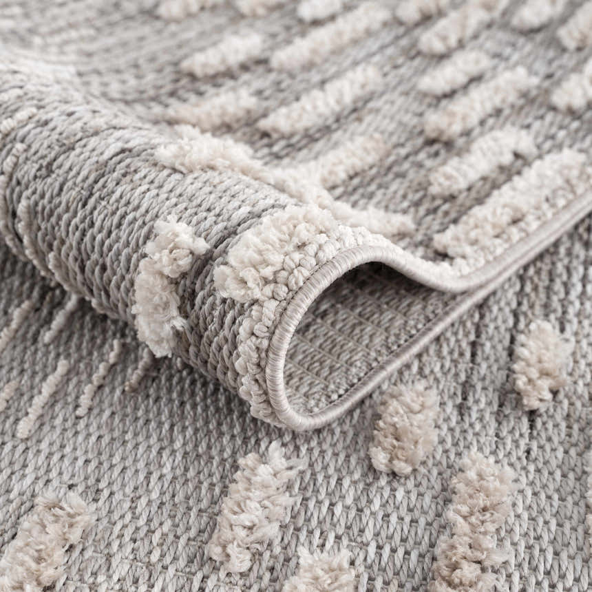 Close up of the Poydras High-Low Rustic Rug showing its gray and beige textured design and machine-woven construction. Fold