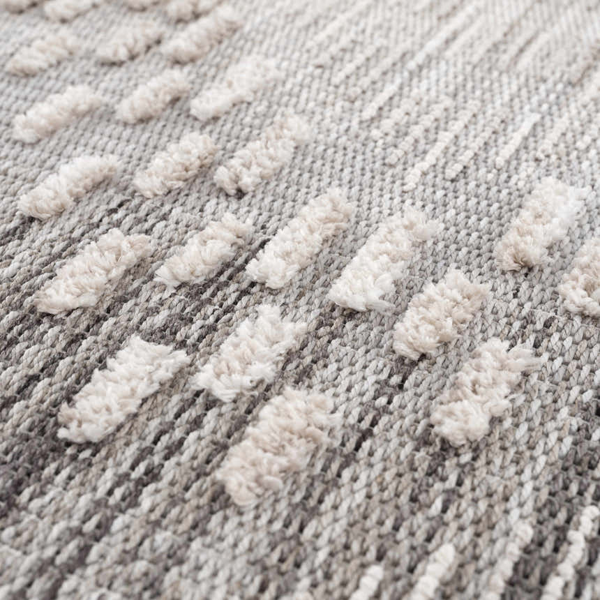 Close-up of the Poydras High-Low Rustic Rug. Features a textured, geometric design in charcoal, gray, and light beige. Texture