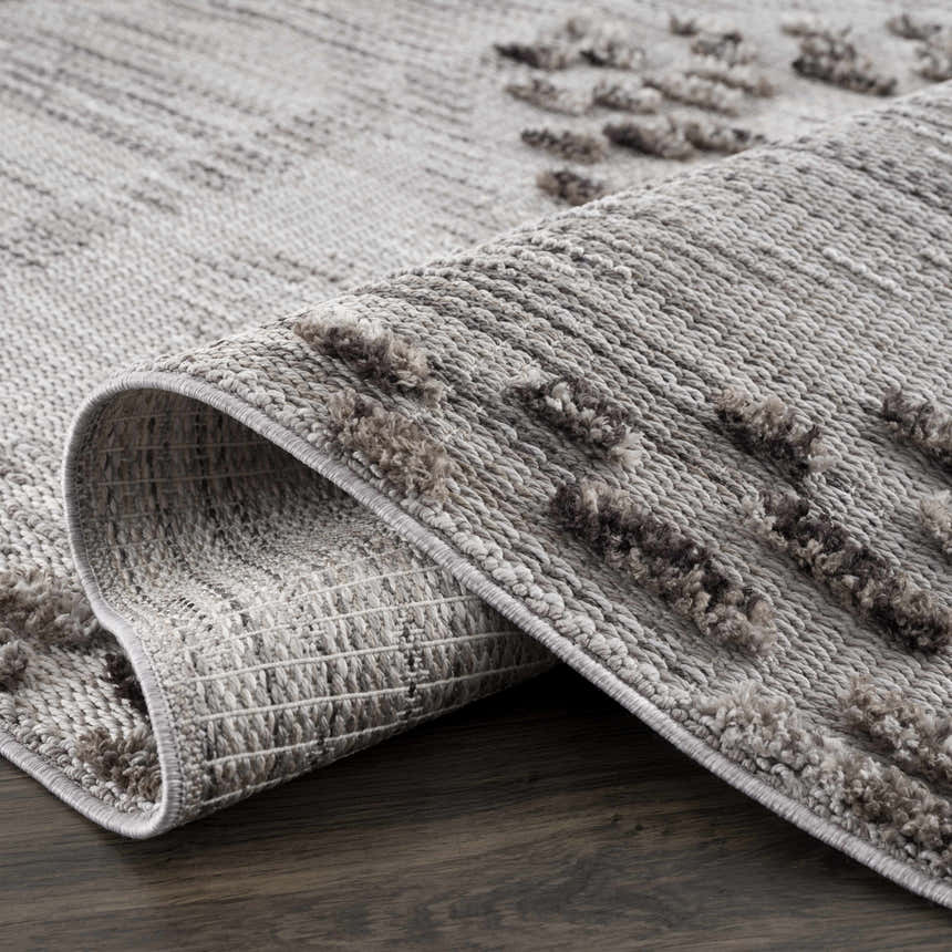 Close-up of the Cabarroguis Area Rug showing its charcoal, cream, and gray geometric pattern and textured, machine-woven construction. Fold