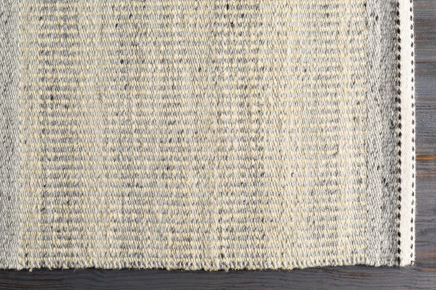 Close-up of the hand-woven Abucay Jute Rug. Charcoal, cream, and light gray jute and wool fibers create a textured look. Corner