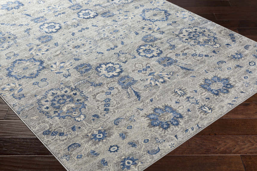 Close-up of the Adairsville Blue Floral Area Carpet, featuring a denim and gray floral pattern on a textured ivory background. Corner