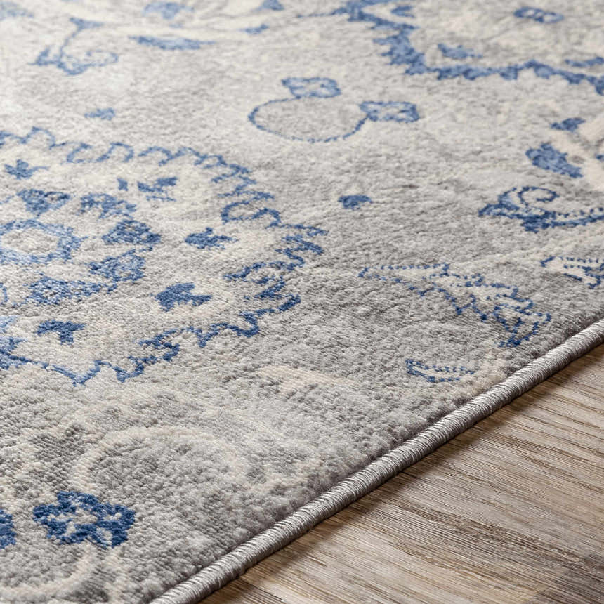 Close-up of the Adairsville Blue Floral Area Carpet showing denim, gray, and ivory floral pattern and machine-woven texture. Texture