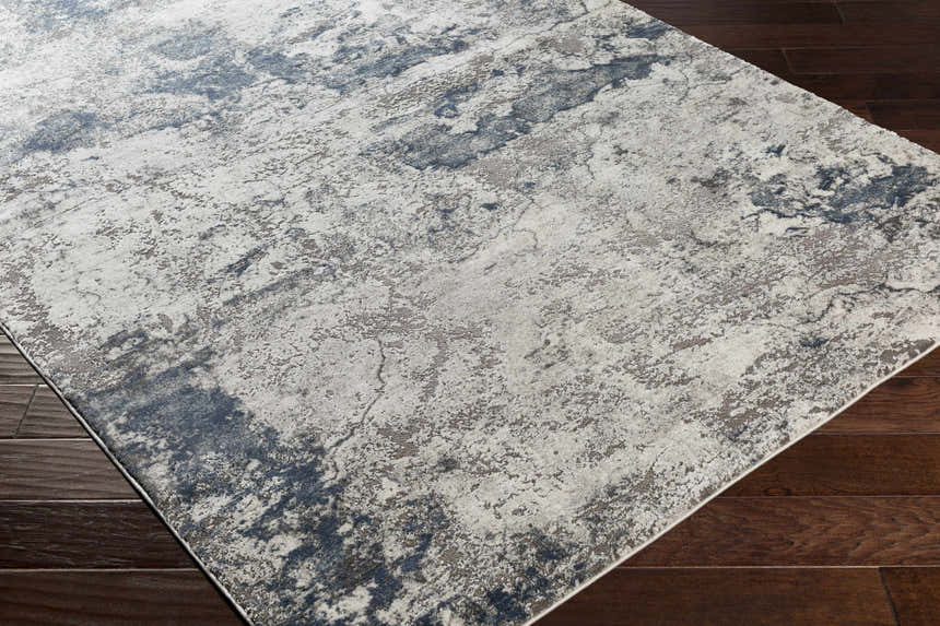 Close-up of the Ainslie Gray Marble Rug. Features a contemporary charcoal, blue, and white abstract pattern. Corner