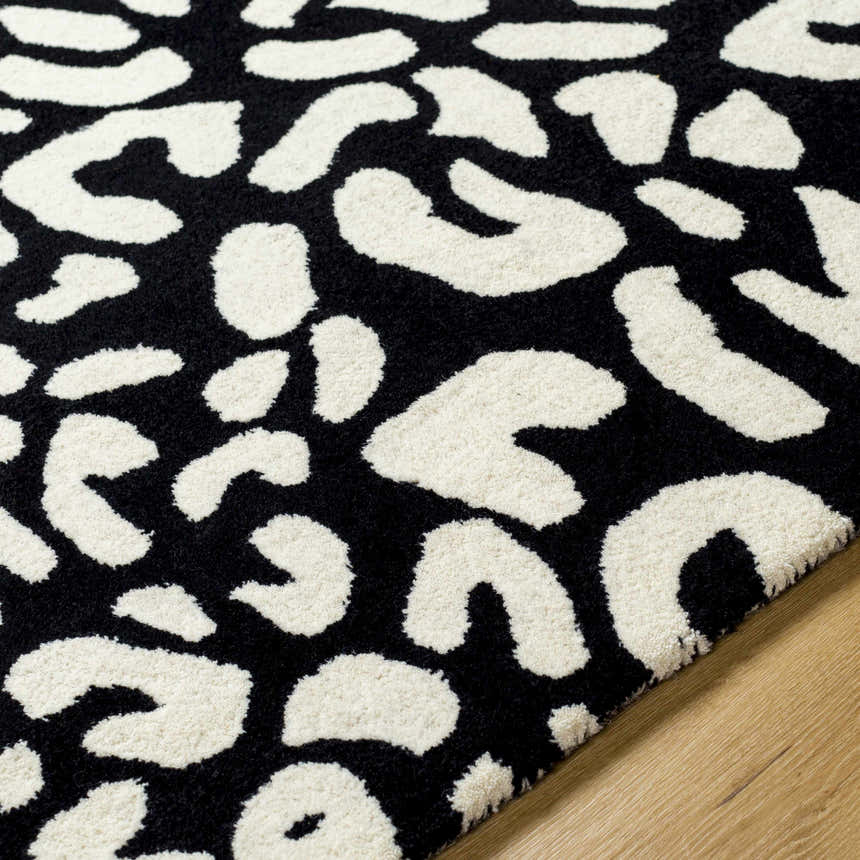 Close-up of the Akeem Leopard Print Area Rug, a hand-tufted wool rug with a black and beige animal print pattern. Texture