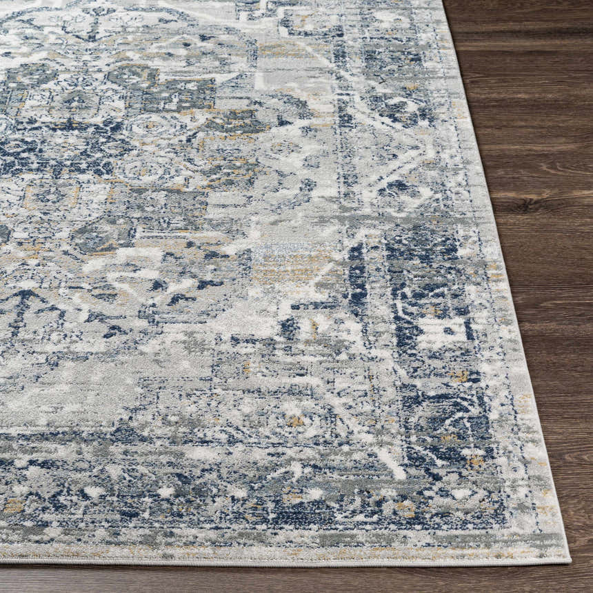 Close-up of the Allerton Area Rug showing its beige, charcoal, dark blue, and gray traditional pattern on dark wood floors. Front