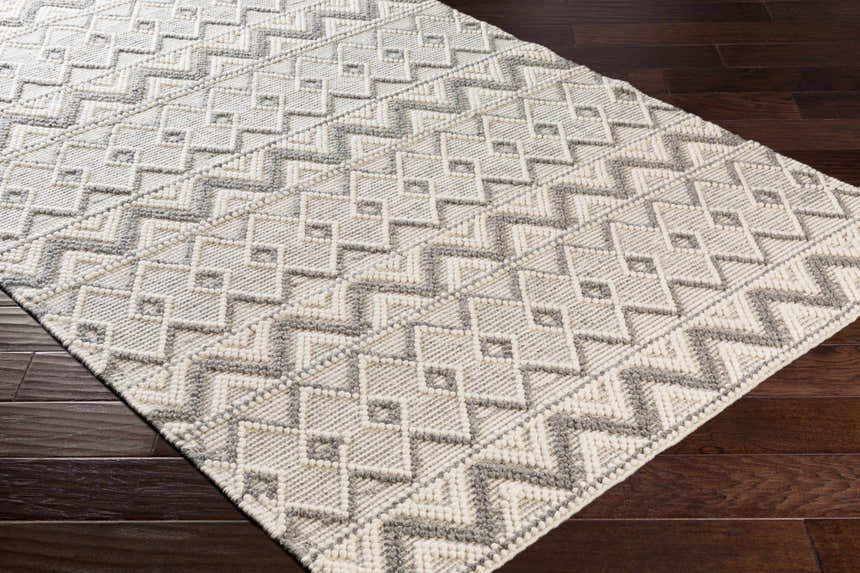 Close-up of the hand woven Whittington Gray&Cream Wool Rug showing its geometric pattern and textured wool on wood floor. Corner
