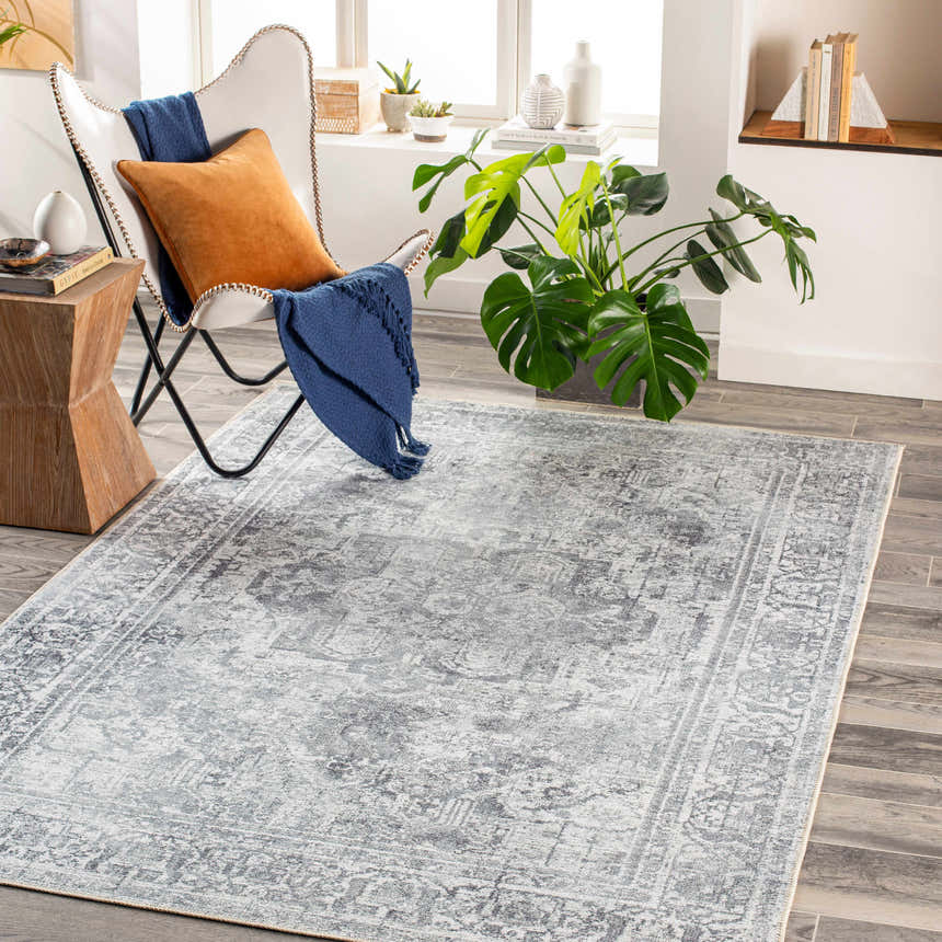 Living room scene with charcoal Aquino Washable Area Rug, white chair, wood floors, and bright natural light. Roomscene-Rectangle