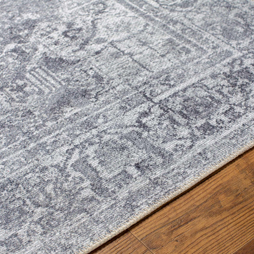 Close-up of the gray Aquino Washable Area Rug showing the traditional pattern and texture on a wood floor. Texture
