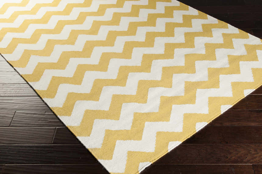 Close-up of the Arvada Area Rug, a hand-woven wool rug with a cream and mustard yellow chevron pattern on dark wood floors. Corner