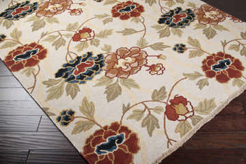 Close-up of Atkins Area Carpet. Beige wool rug with brick red, blue, and brown floral pattern on dark wood floor. Corner