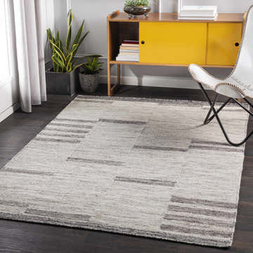 Living room scene with a charcoal and cream Auchinleck Area Rug, yellow cabinet, white chair, and dark wood floors. Roomscene-Rectangle