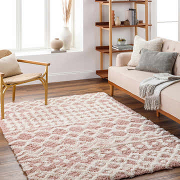 Living room scene with a pink and white geometric Azura Shag Area Rug, beige sofa, wood floors, and natural light. Roomscene-Rectangle