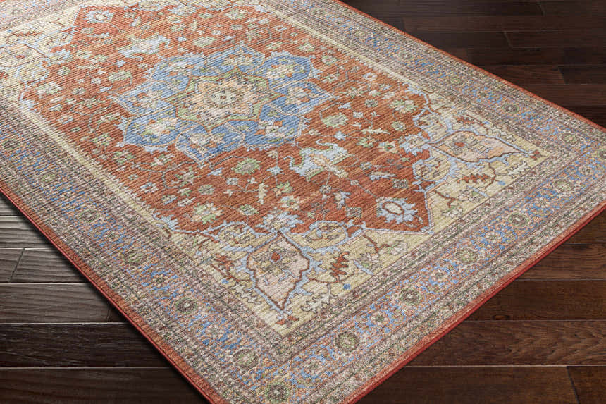 Bacoor Washable Area Rug on dark wood floor. Traditional oriental rug with brick red, beige, and blue floral pattern. Corner