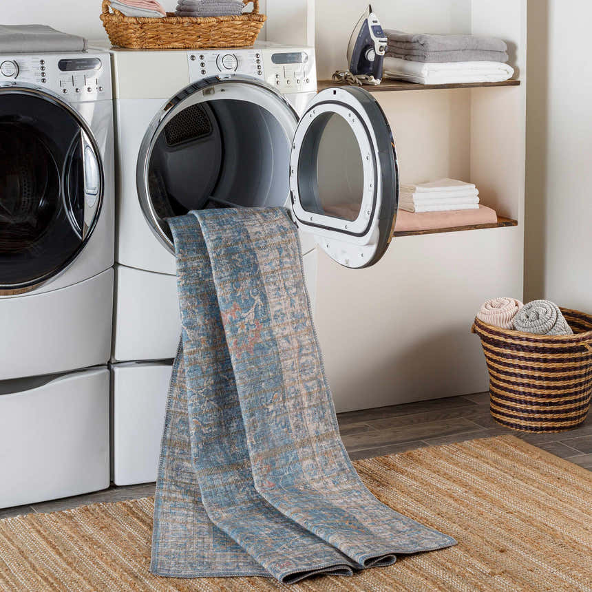Laundry room scene with blue Bagontapay Washable Area Rug coming out of the dryer, layered over a jute rug. Washing-Machine