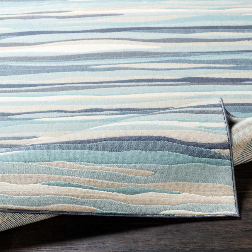 Close up of the Basco Area Rug featuring aqua, charcoal, beige, and blue wavy stripes. Fold