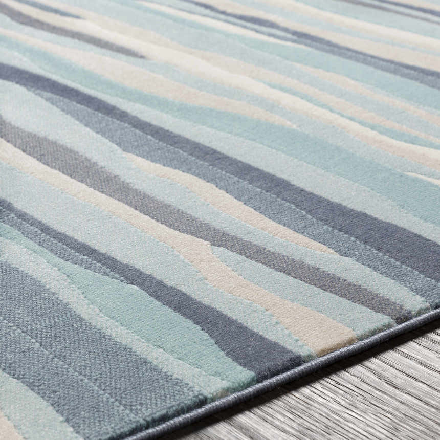 Close-up of the Basco Area Rug showing its aqua, charcoal, beige, and blue wavy stripe pattern and soft texture. Texture