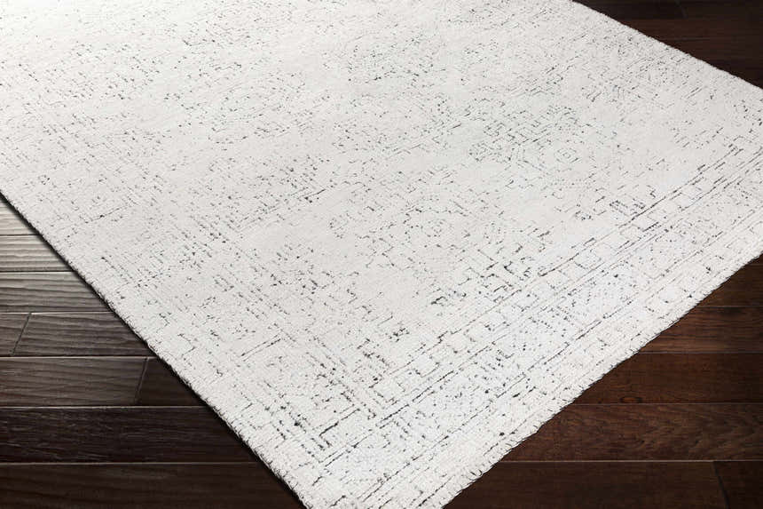 Close-up of the Blackfoot Area Rug showing its white and black farmhouse design and hand-knotted texture on dark wood floors. Corner