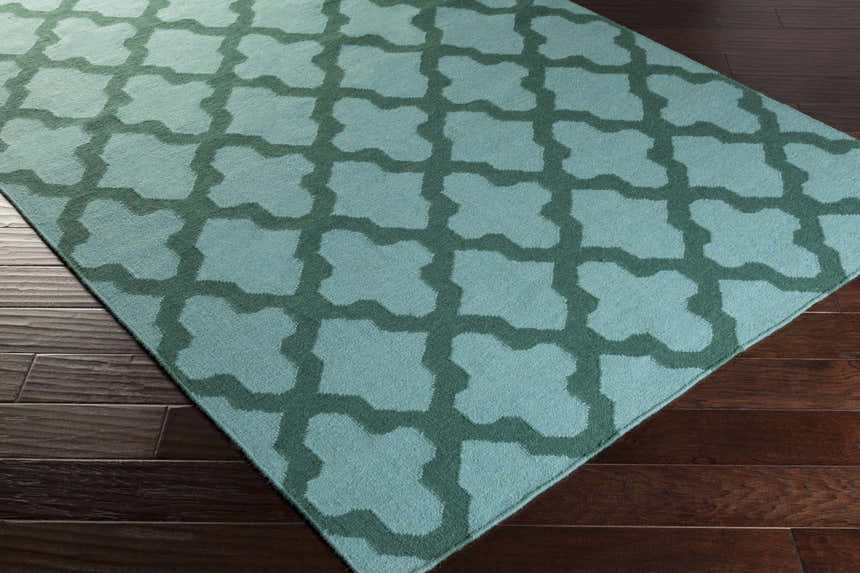 Close-up of the Boles Area Carpet. Sky blue wool rug with a teal quatrefoil pattern on dark wood floors. Corner
