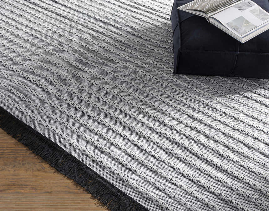 Close-up of the hand-woven Brockman Area Rug. Black fringe, gray and off-white stripes, with a textured, contemporary pattern. Styleshot