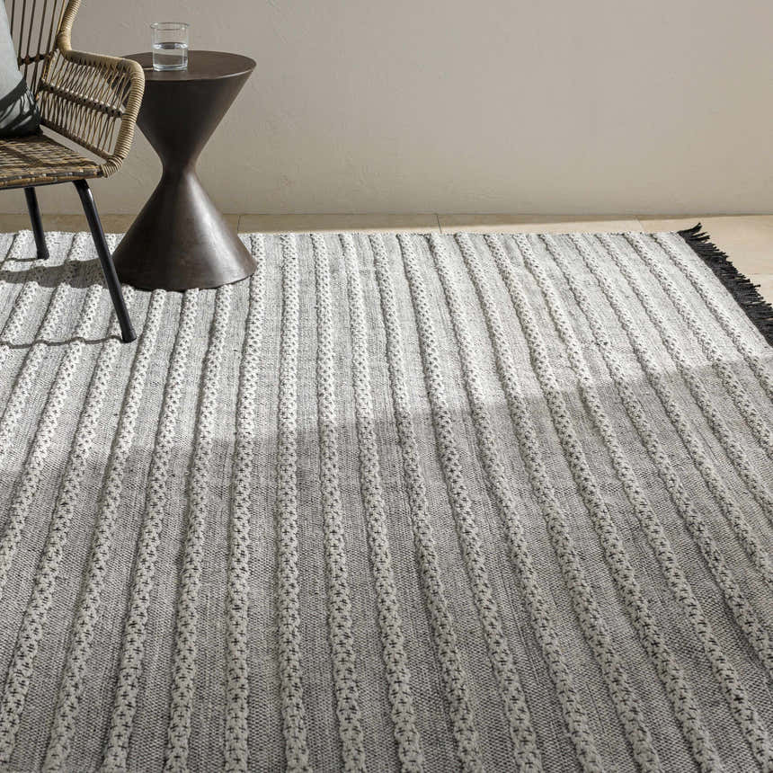 Neutral room scene with a gray and off-white striped Brockman Area Rug, woven chair, and small accent table. Styleshot